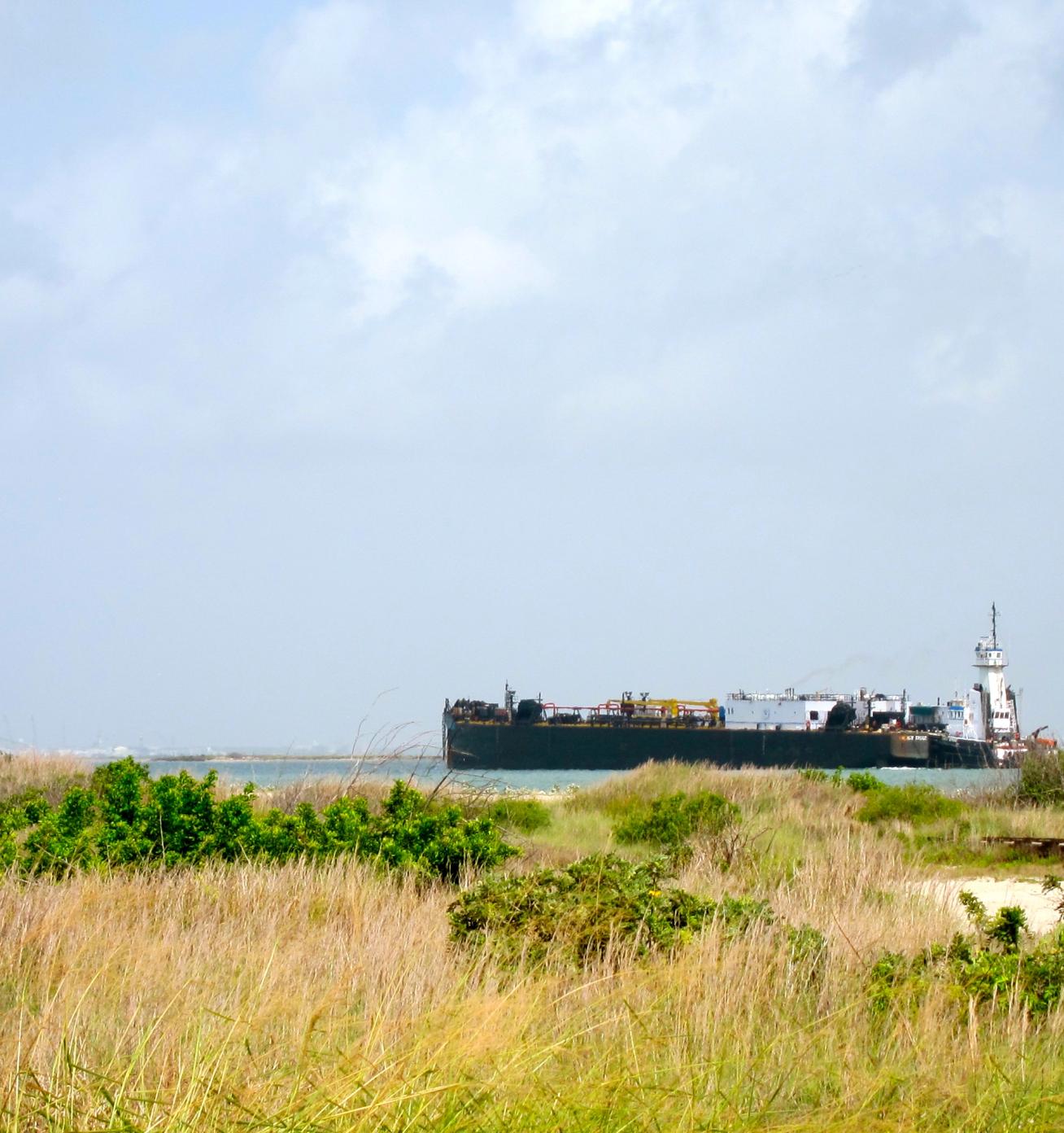 Barge in the distant ocean past sand dunes