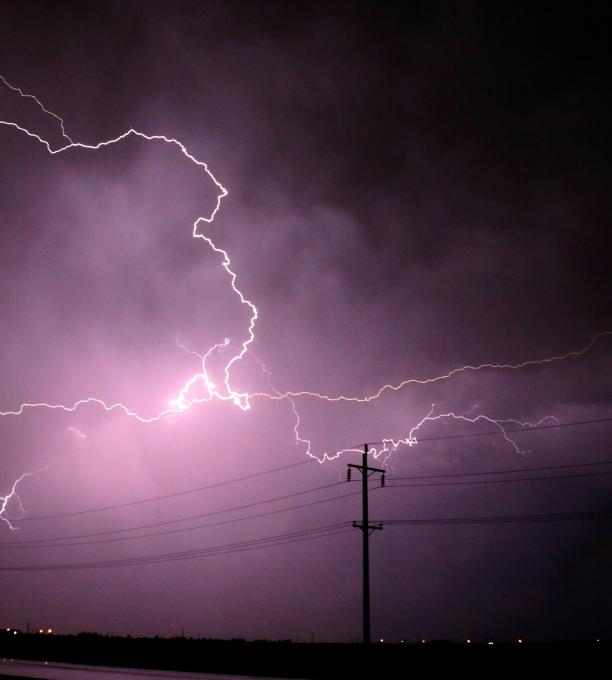 Lightning in a dark sky behind a power line.