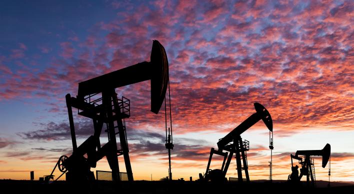 3 Silhouettes of oil pump jacks stand against a vibrant sunset sky with scattered clouds.