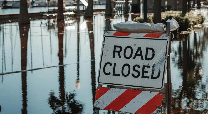 A flooded street with a road closed sign and sand bags.