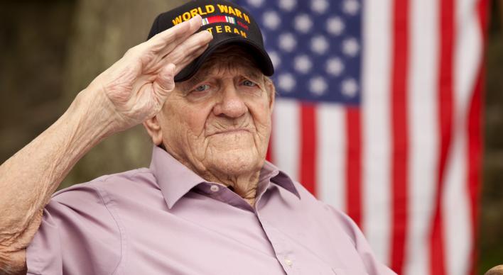 A WWII veteran salutes the camera with a US flag in background.