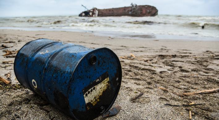 Shipwrecked tanker with an oil barrel in the foreground.