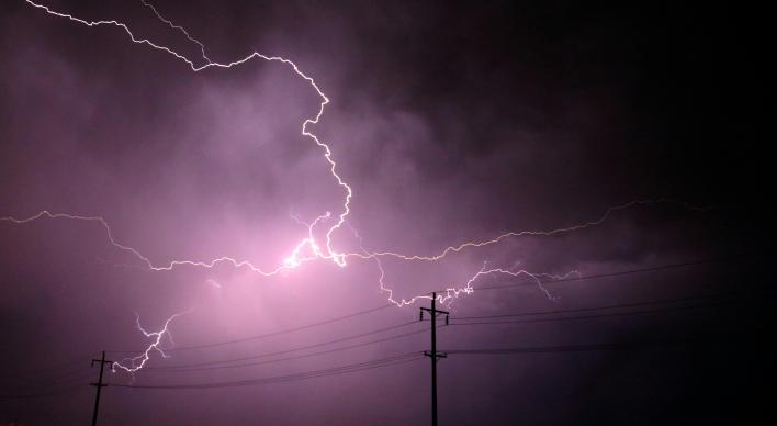 Lightning in a dark sky behind a power line.