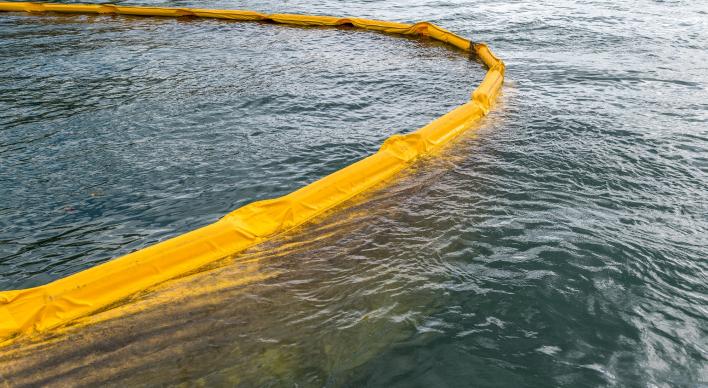 A yellow oil spill barrier contains an oil spill in the ocean