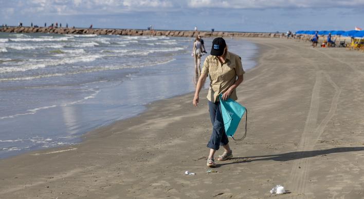 Commissioner Dawn Buckingham M.D. picking up trash in a Texas Adopt-A-Beach hat.