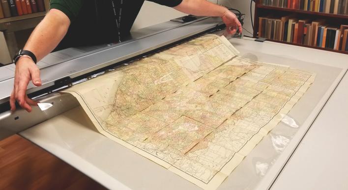A scan lab employee feeding a original map through a large image scanner